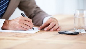 Cropped image of a businessman writing on a piece of paper with his cellphone in front of him